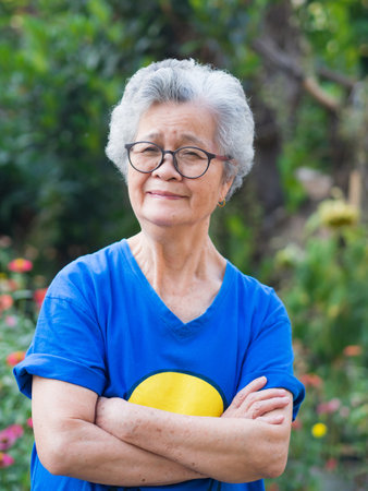 Happy a senior woman with short gray hair smiling, arms crossed, and looking at the camera standing in a garden. Concept of aged people and relaxation.の写真素材