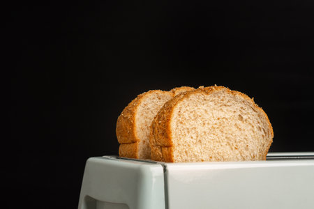 Rich and soft whole wheat bread in the toaster with a black background. Close-up photo. Space for text.の写真素材