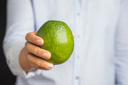 Hand holding green avocado while standing in the studio. Natural fresh organic exotic fruit. Healthy...