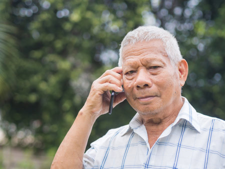 Happy a senior man using a smartphone, smiling and looking at the camera while standing in a garden. Space for text. Aged people and communication concept.の写真素材