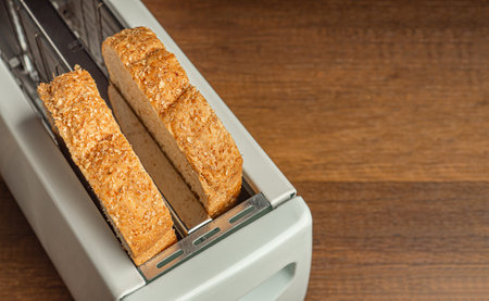Rich and soft whole wheat bread in the toaster on wooden table background. Close-up photo. Space for text.の写真素材
