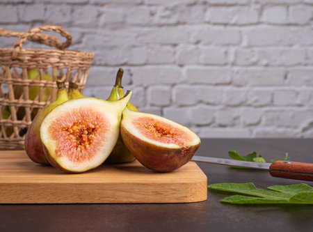 Ripe figs fruit are on a wooden cutting board and a bamboo basket with white brick wall background....