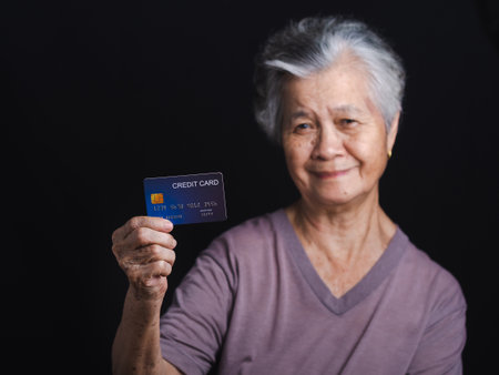 Portrait of a senior woman with short gray hair holding a blue credit card and looking at the camera...