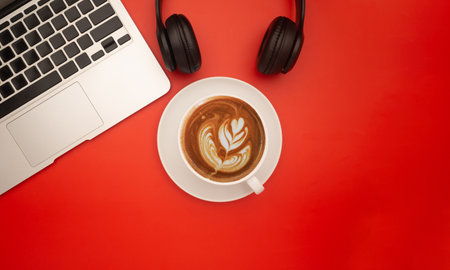 Top view of a laptop, headphones, and a coffee cup isolated on a red background with space for text.の写真素材
