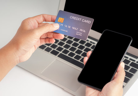 Close-up of hand holding a credit card and smartphone for shopping online with a laptop. Business,...