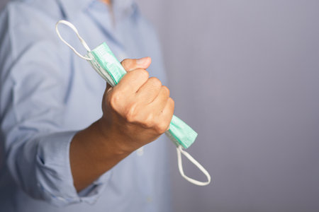 The end of COVID 19 pandemic. End lockdown back to Normal life. Man hand holds a medical mask in his fists. Victory hand mask. A symbol of the end of pandemic virus disease.の写真素材