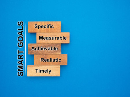 SMART Goal setting for business. Pieces of wood with text-specific, measurable, achievable, realistic, and timely isolated on a blue background. Space for text. Business strategy concept.の写真素材