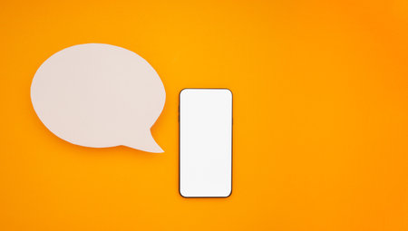 Top view of a blank white speech bubble and a mobile phone isolated on a yellow background. Phone message. Advertisement idea. Empty speech balloon for advertising.の写真素材