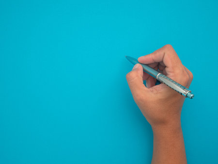Hand woman holding of a pen on a blue background. Space for text. Top view.の写真素材