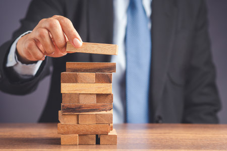 Risk of management and strategy plans for business growth and success concept. Close-up hand of the businessman in a suit playing a wooden block game while sitting at the work table. Space for text.の写真素材