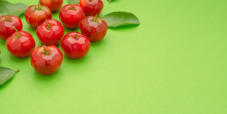 Pile of ripe red acerola cherries and green leaves isolated on a light green background. High vitamin C and antioxidant fruits. Top view. Space for text. Close-up photo. Healthy fruits concept.の写真素材