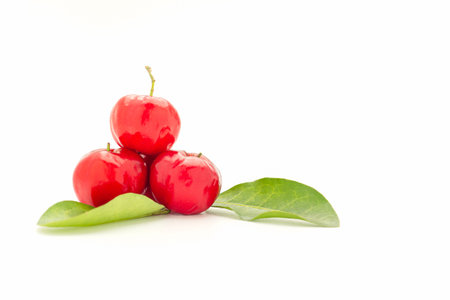 Pile of ripe red acerola cherries and green leaves isolated on a white background.の写真素材
