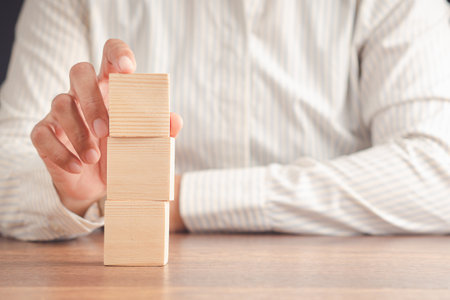 Businessman arranging a blank wooden cube on a wooden table while sitting in the office. Space for textの写真素材