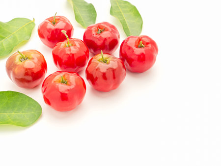 Pile of ripe red acerola cherries and green leaves isolated on a white background. High vitamin C and antioxidant fruits. Top view. Space for text. Close-up photo. Healthy fruits conceptの写真素材