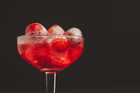 Wine glass with cherry juice against a black background. Refreshing cold drink. Summer party. Ripe red acerola cherries and green leaves on a table. High vitamin C fruitsの写真素材