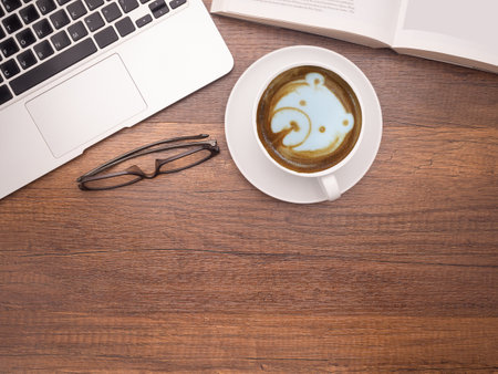 Working desk table concept. Top view of a laptop, a book, glasses, and a coffee cup on a wooden table in the office. Flat lay. Space for textの写真素材