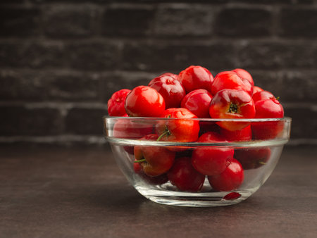 Red acerola cherry in a bowl glass with a black brick wall background. High vitamin C and antioxidant fruits. Space for text. Healthy fruits conceptの写真素材