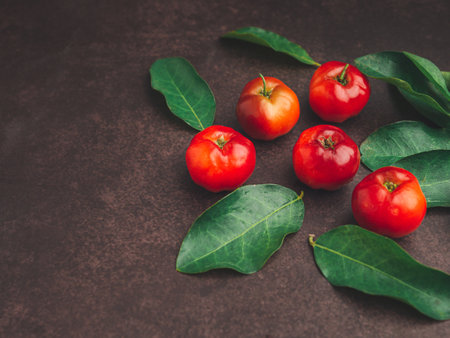 Overhead view of ripe red acerola cherries and green leaves scattered on a table. High vitamin C and antioxidant fruits. Space for text. Healthy fruits conceptの写真素材