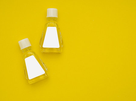 Small bottle containers with yellow herbal. Blank label for branding mockup. Natural beauty and health product concept. Top view. Flat lay on yellow backgroundの写真素材
