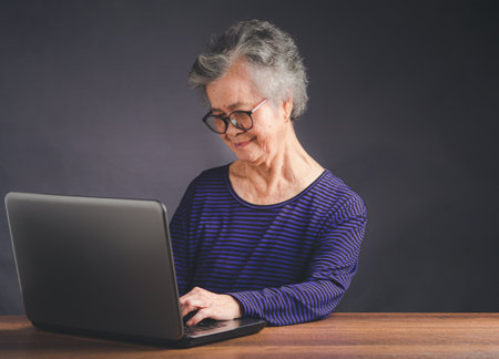 Portrait of an elderly Asian woman with short gray hair using a laptop for searching data on the...