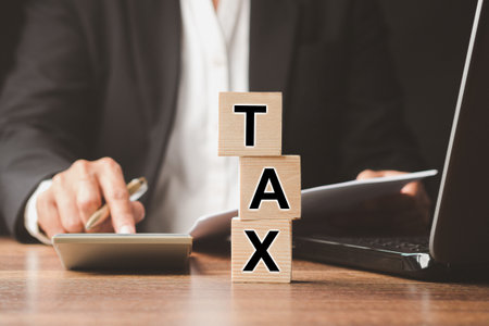 Wooden cubes with letters "TAX" on a wooden table. Tax payment and Calculation tax return concept. Businessman in a suit using a calculator and individual income tax payment formの写真素材