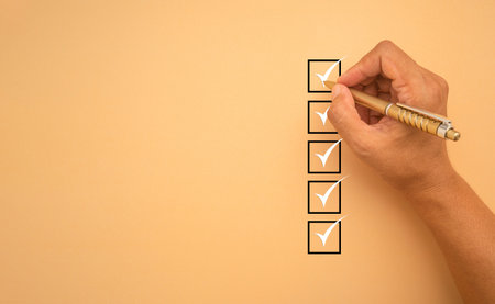 Checklist concept. White marking on checklist box isolated on an orange background. Hand holding a...