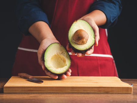 Close-up of hands holding a fresh avocado while standing in the kitchen. Healthy fruit and food...