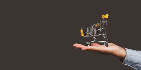 Business and e-commerce concept. Close-up of an empty yellow shopping trolley on the palm people while standing on gray background in the studio. Side view. Space for text.の写真素材
