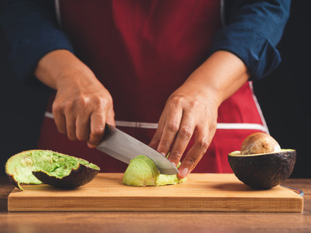 Chef slicing avocado on a wooden cutting board with the knife. Healthy fruit and food eating concept. Close-up photoの写真素材