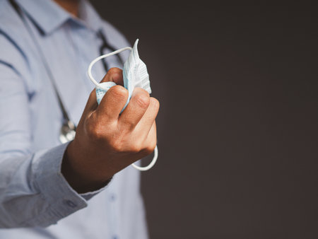 The doctor's holding a medical mask in his fist. End of quarantine. A symbol of the end of pandemic virus disease. Victory hand mask. Space for text. Close-up photoの写真素材