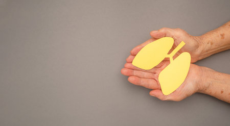 Lungs shape made from yellow paper on a palm old woman on a gray background. World tuberculosis day, world no tobacco day, lung cancer, pulmonary hypertension, pneumoniaの写真素材