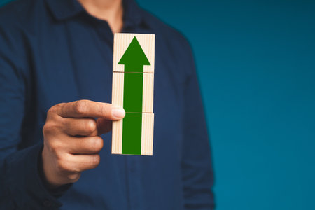 Business growth process and achieving the goal. Businessman holding wooden cubes with arrow up while...