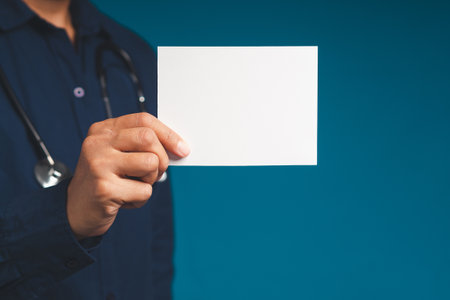 Doctor hand holding a blank white paper while standing on a blue background. Space for text. Medical and information conceptの写真素材