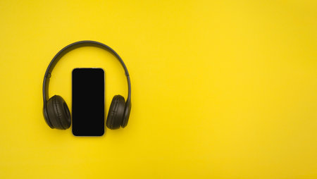 Top view of a smartphone and headphones over yellow background. Space for text. Communication and entertainment conceptの写真素材