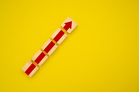 Wooden blocks with red arrow up over a yellow background. Business growth and strategy concept. Top view. Space for textの写真素材