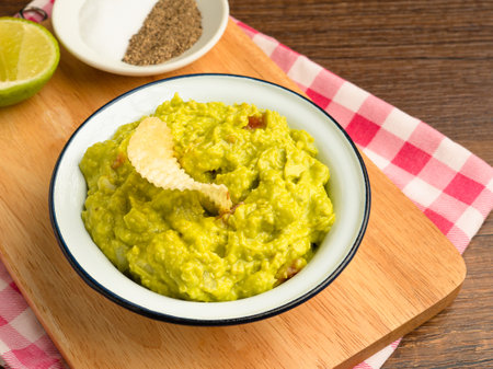 Top view of fresh guacamole in a bowl on a wooden cutting board. Healthy avocado spread. Flat lay. Concept of traditional Mexican preparationの写真素材