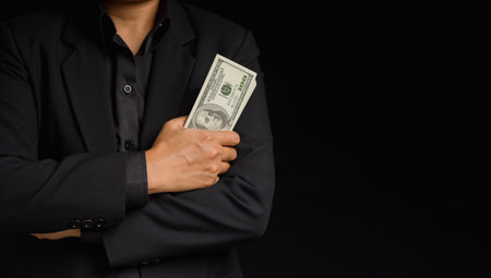 Business and finance concept. Businessman in suit holding US banknotes while standing in the studio with a black background. Personal loans and payday loans. Space for textの写真素材