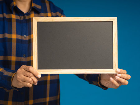 Hand holding of a small blackboard while standing over a blue background. Space for text. Close-up photoの写真素材