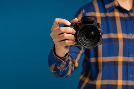Photographer with a camera. Close-up of hand holding the digital camera while standing on a blue background. Space for textの写真素材