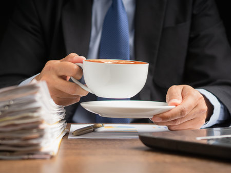 Businessman hand holding a cup of coffee sitting working at the office. Close-up photo. Beverage and relaxation conceptの写真素材