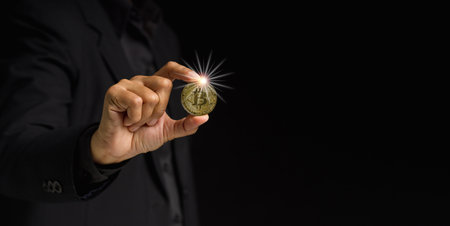 Businessman holding a bitcoin coin while standing over a black background. Bitcoin is a symbol of cryptocurrency, electronic virtual money. Blockchain technology, payment, and digital asset conceptの写真素材