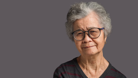Portrait of a senior woman with short gray hair looking at the camera with a smile while standing on gray background in the studio. Aged people and relaxation conceptの写真素材
