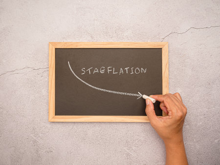 Hand draws an arrow of stagflation with chalk on a blackboard. Stagnating economy with high inflation rates, depreciation of moneyの写真素材