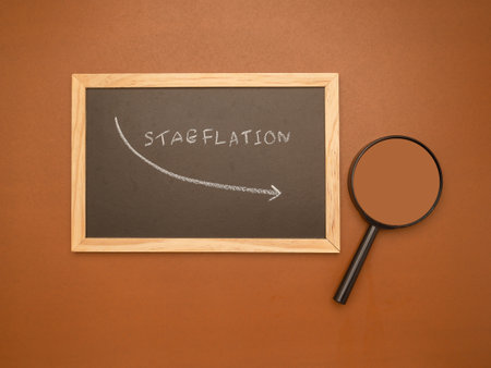 Hand draws an arrow of stagflation with chalk on a blackboard and magnifying glass over a brown background. Stagnating economy with high inflation rates, depreciation of moneyの写真素材