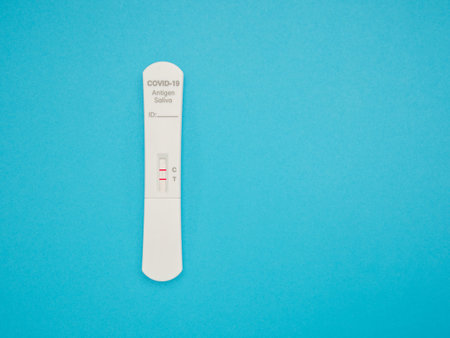 Covid-19 Positive test result with SARS-COV-2 Saliva Antigen Rapid Test Kit (ATK) over a blue...