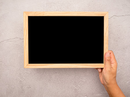 Hand holding of a mini blank blackboard with a wooden border over a cement floor. Space for text. Top viewの写真素材