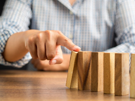 Risk and strategy in business concept. Close-up of hand pushing a wooden block on a line of dominos while sitting in the office. Close-up photoの写真素材