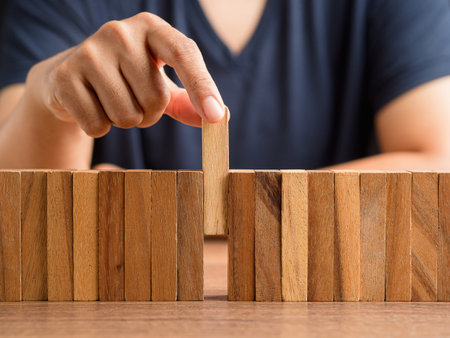 Business planning, risk, and crisis management concept. A businessman in a black shirt picking one wooden block from many wooden blocks in a row on the deskの写真素材