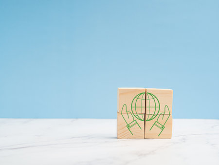 Save Earth Concept. Wooden cubes with the world green icons and two hands over a marble floor against a blue background. Earth in hands. Space for textの写真素材