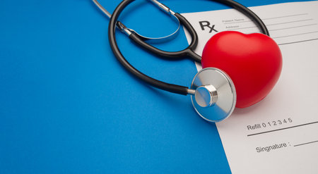 Top view of a stethoscope and a red heart shape over the medical prescription sheet on a blue...